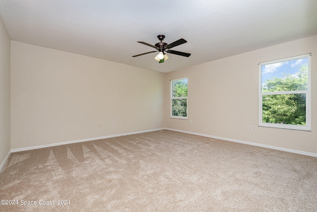 spare room with ceiling fan, light colored carpet, and a wealth of natural light