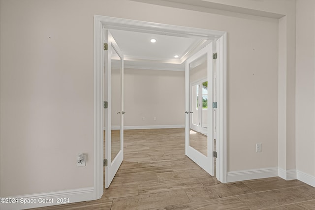 corridor featuring crown molding, light hardwood / wood-style floors, french doors, and a raised ceiling