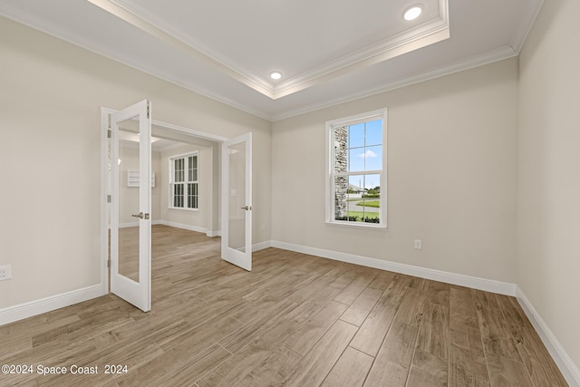 spare room featuring ornamental molding, light wood-type flooring, a raised ceiling, and french doors