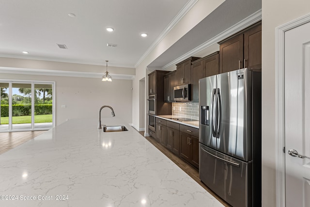 kitchen with pendant lighting, sink, ornamental molding, appliances with stainless steel finishes, and light stone countertops