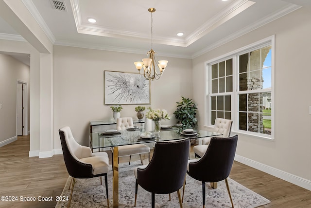 dining space featuring wood-type flooring, ornamental molding, and a raised ceiling