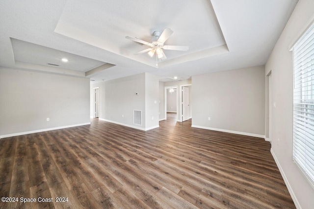 unfurnished living room with a raised ceiling, ceiling fan, dark wood-type flooring, and a textured ceiling