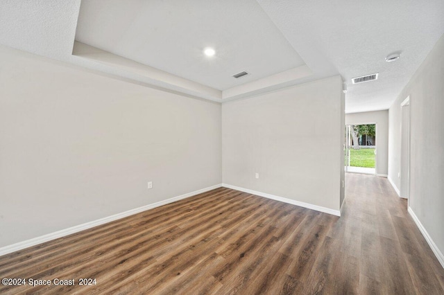 unfurnished room featuring a tray ceiling, dark wood-type flooring, and a textured ceiling