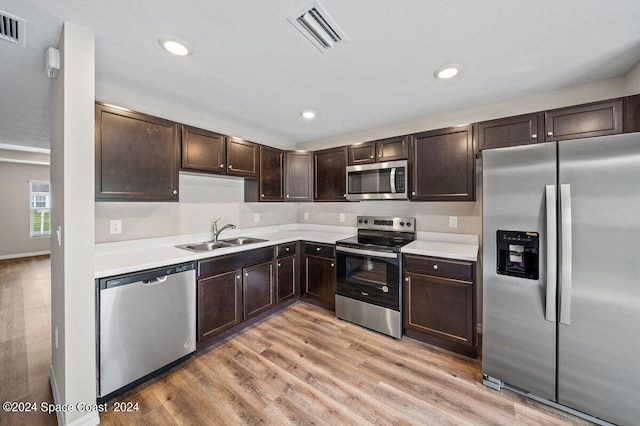 kitchen featuring sink, stainless steel appliances, a textured ceiling, dark brown cabinets, and light wood-type flooring