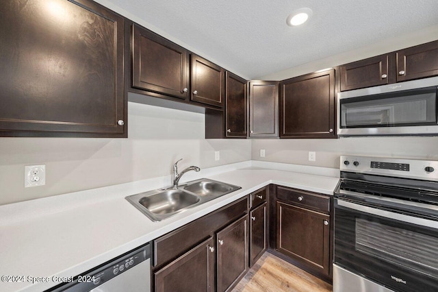 kitchen with sink, light wood-type flooring, a textured ceiling, appliances with stainless steel finishes, and dark brown cabinetry