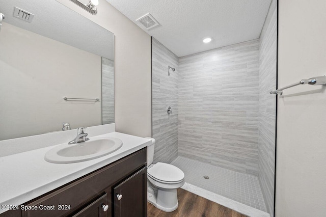 bathroom with a textured ceiling, tiled shower, toilet, vanity, and hardwood / wood-style flooring