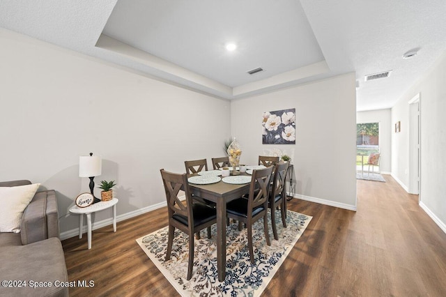 dining space featuring a raised ceiling, dark hardwood / wood-style flooring, and a textured ceiling