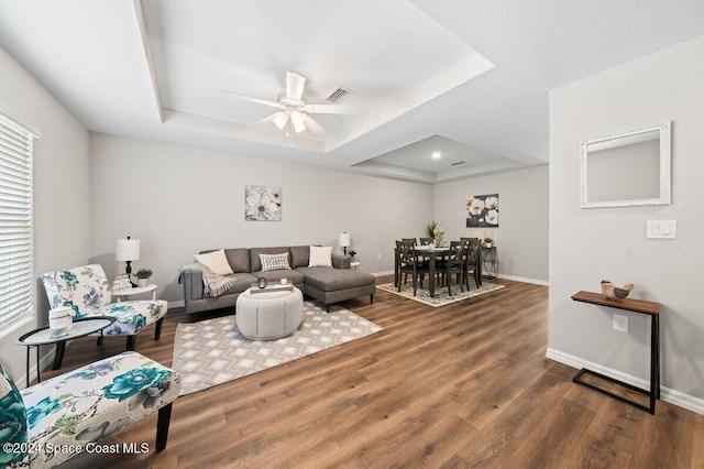 living room featuring ceiling fan, a raised ceiling, and dark wood-type flooring