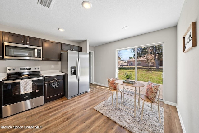 kitchen with dark brown cabinetry, stainless steel appliances, a textured ceiling, and light hardwood / wood-style floors