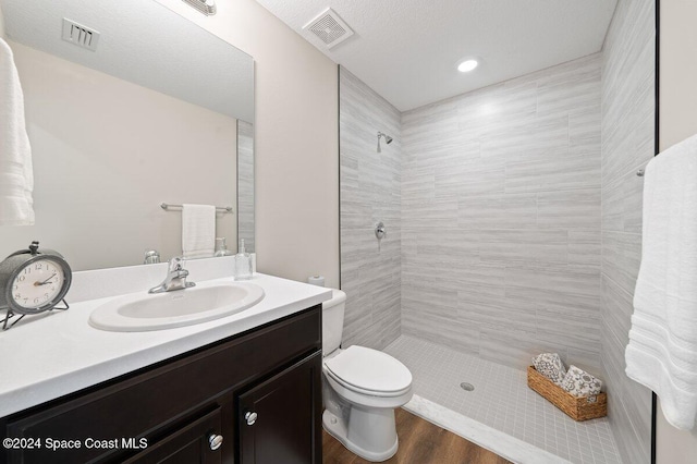 bathroom with tiled shower, vanity, hardwood / wood-style flooring, and toilet