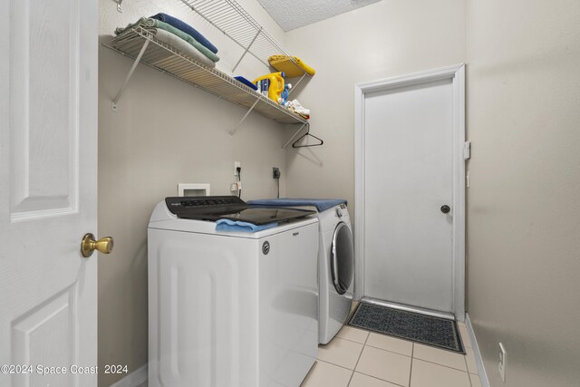 laundry area featuring light tile patterned floors, washer and dryer, and a textured ceiling