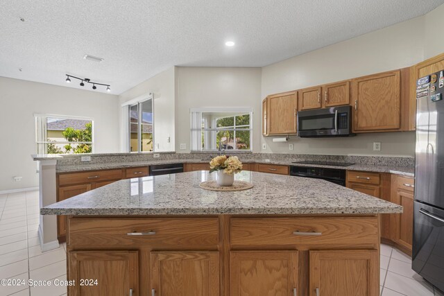 kitchen featuring light tile patterned floors, a textured ceiling, a kitchen island, and black appliances