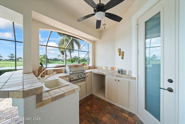 view of patio featuring ceiling fan, sink, grilling area, a lanai, and exterior kitchen