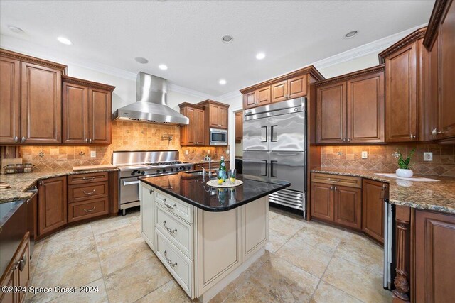 kitchen with dark stone countertops, built in appliances, and wall chimney range hood