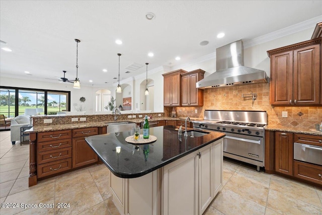 kitchen featuring hanging light fixtures, an island with sink, high end stove, wall chimney exhaust hood, and sink