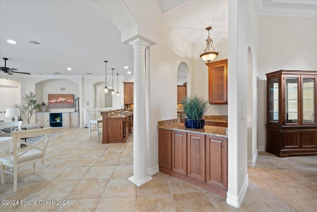 interior space with ceiling fan, ornamental molding, decorative light fixtures, decorative columns, and a breakfast bar area