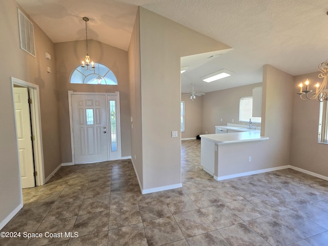 entrance foyer featuring ceiling fan with notable chandelier, sink, light tile patterned floors, a textured ceiling, and high vaulted ceiling