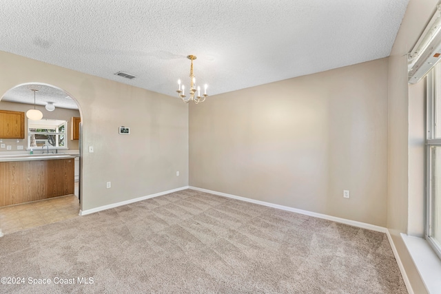 carpeted spare room with a notable chandelier and a textured ceiling