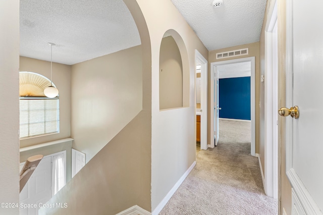 hall with light carpet and a textured ceiling