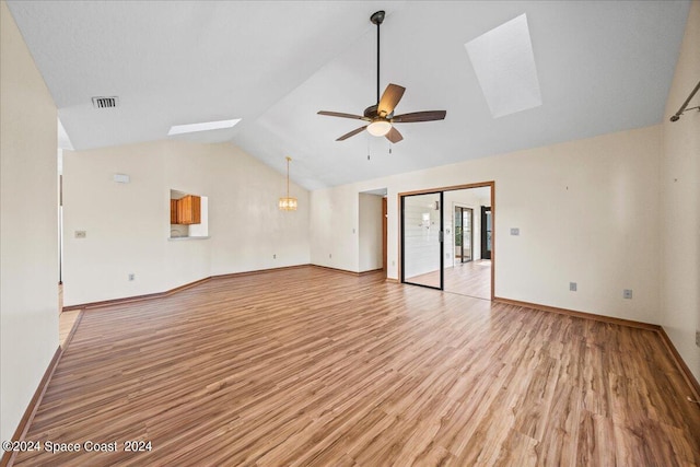 unfurnished living room with ceiling fan with notable chandelier, vaulted ceiling with skylight, and light hardwood / wood-style flooring