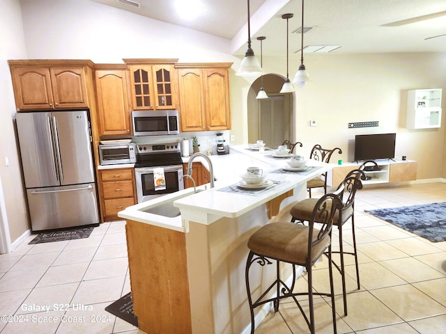 kitchen featuring pendant lighting, lofted ceiling, kitchen peninsula, appliances with stainless steel finishes, and a breakfast bar