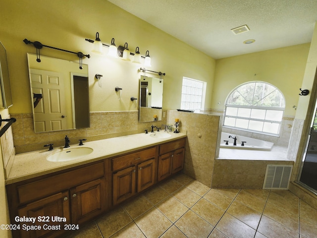 bathroom featuring tile walls, tiled bath, vanity, a textured ceiling, and tile patterned flooring