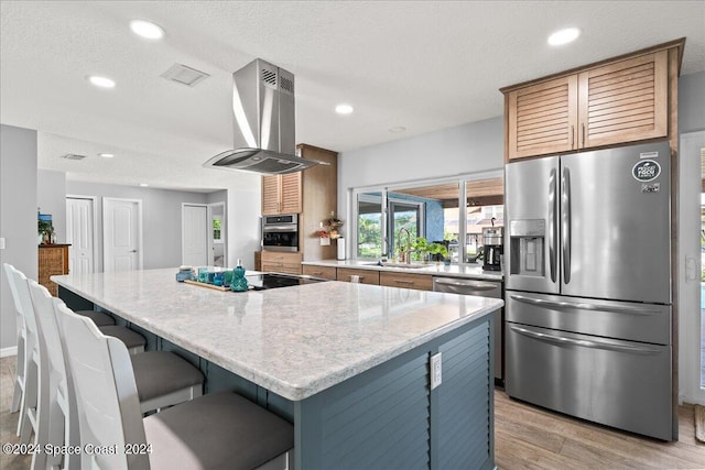 kitchen with sink, appliances with stainless steel finishes, a kitchen island, light stone counters, and island exhaust hood