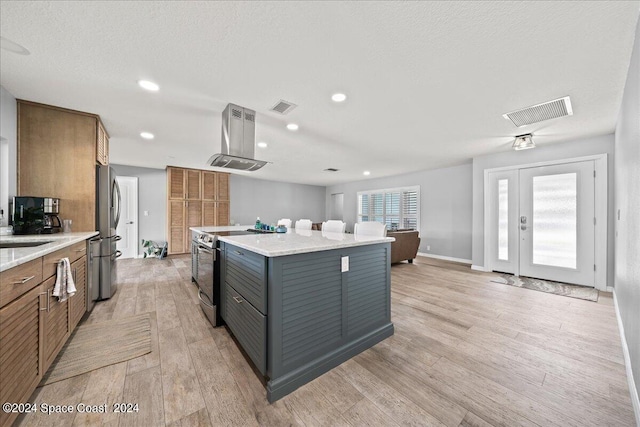 kitchen featuring light wood-type flooring, light stone counters, stainless steel appliances, a center island, and range hood