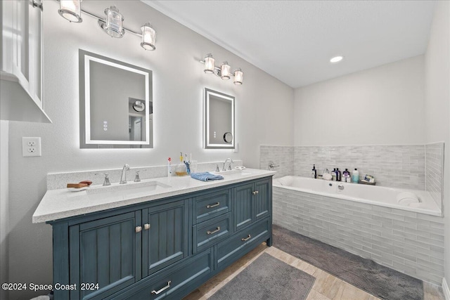 bathroom with vanity, hardwood / wood-style flooring, and tiled tub