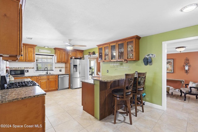 kitchen with a kitchen bar, stainless steel appliances, sink, stone countertops, and kitchen peninsula