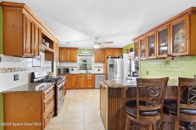 kitchen with sink, a kitchen bar, dark stone counters, and appliances with stainless steel finishes