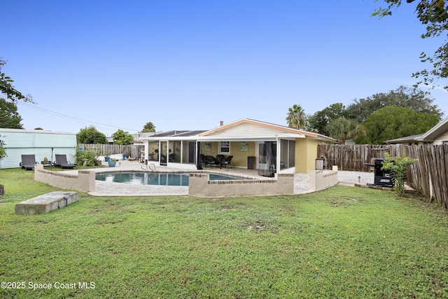 back of property with a fenced in pool, a patio area, a lawn, and solar panels