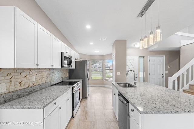 kitchen featuring hanging light fixtures, sink, white cabinetry, appliances with stainless steel finishes, and light stone countertops