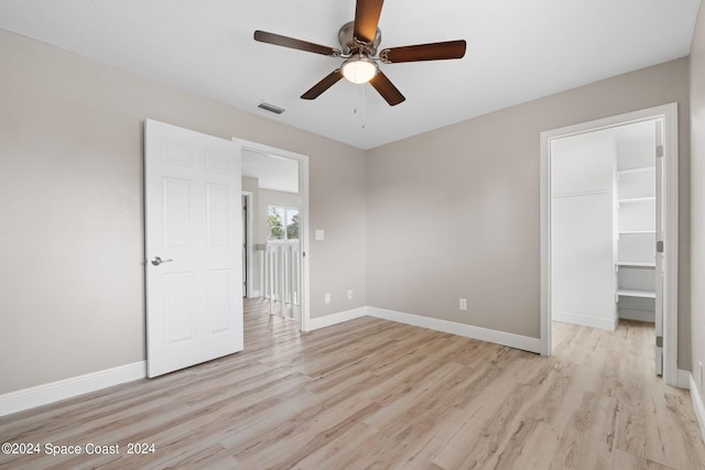 unfurnished bedroom featuring ceiling fan, light hardwood / wood-style flooring, a closet, and a walk in closet