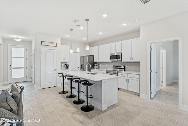 kitchen featuring pendant lighting, a kitchen island with sink, stainless steel appliances, and white cabinetry