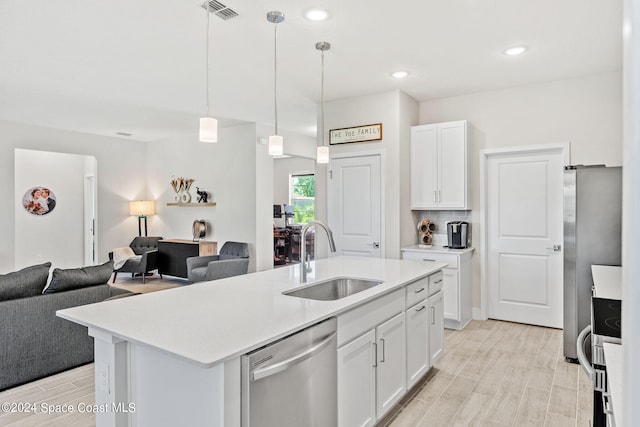 kitchen featuring stainless steel appliances, sink, pendant lighting, white cabinetry, and a center island with sink