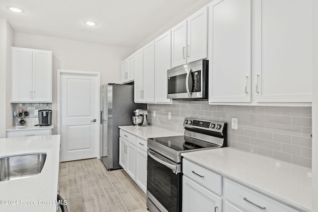 kitchen with light hardwood / wood-style floors, sink, decorative backsplash, white cabinets, and appliances with stainless steel finishes