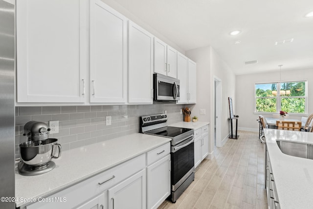 kitchen featuring white cabinets, stainless steel appliances, sink, and decorative light fixtures