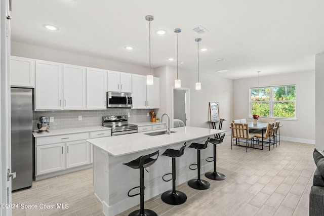 kitchen with stainless steel appliances, an island with sink, decorative light fixtures, and white cabinetry