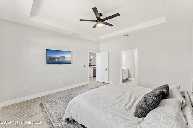 bedroom featuring a raised ceiling, connected bathroom, light wood-type flooring, and ceiling fan