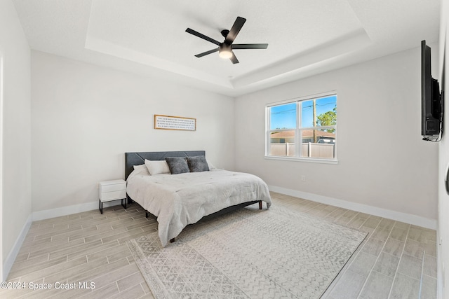 bedroom featuring ceiling fan, a tray ceiling, and light wood-type flooring