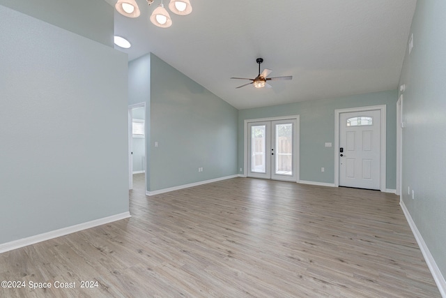 unfurnished living room featuring light wood-type flooring, high vaulted ceiling, french doors, and ceiling fan with notable chandelier