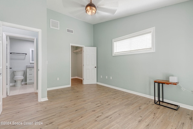 unfurnished bedroom featuring connected bathroom, a closet, light wood-type flooring, ceiling fan, and a spacious closet