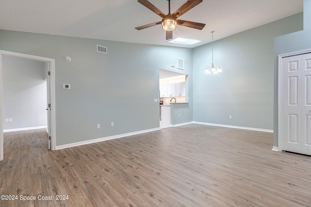 empty room with ceiling fan with notable chandelier, lofted ceiling with skylight, and light hardwood / wood-style flooring