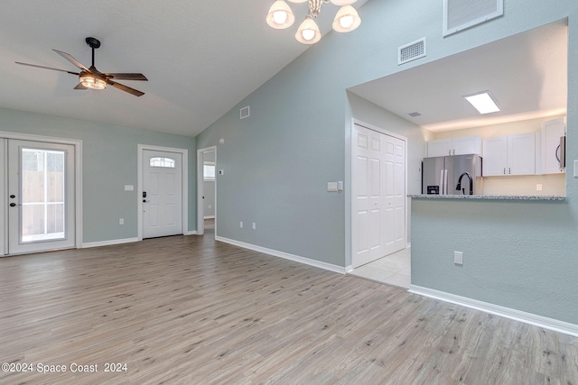 unfurnished living room with ceiling fan with notable chandelier, light wood-type flooring, and vaulted ceiling