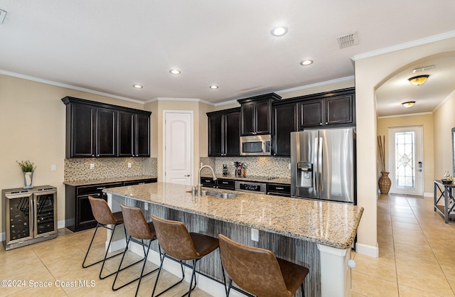 kitchen with appliances with stainless steel finishes, ornamental molding, sink, wine cooler, and an island with sink