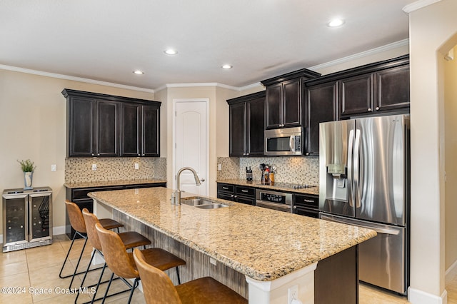 kitchen featuring light stone counters, ornamental molding, stainless steel appliances, sink, and an island with sink