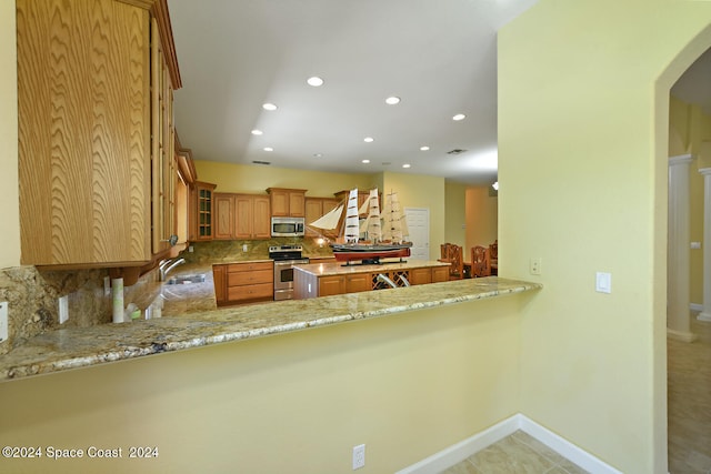 kitchen featuring light stone counters, tasteful backsplash, sink, kitchen peninsula, and appliances with stainless steel finishes