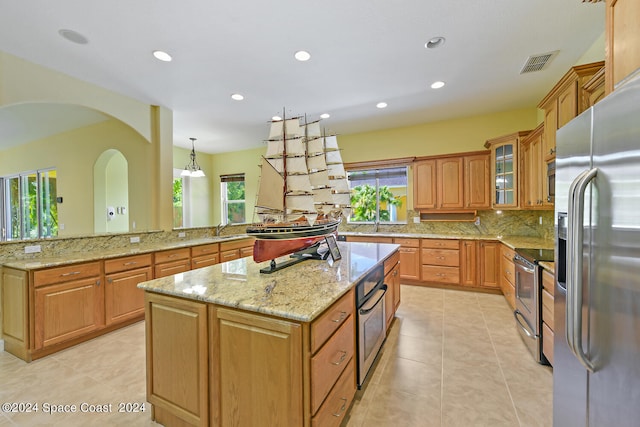 kitchen featuring a kitchen island, appliances with stainless steel finishes, hanging light fixtures, and a wealth of natural light