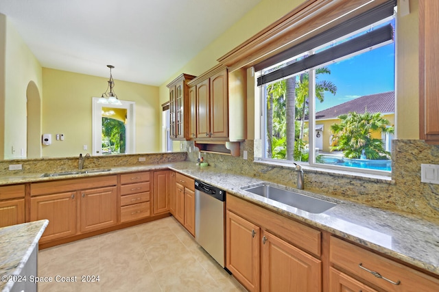 kitchen with light stone countertops, sink, hanging light fixtures, and stainless steel dishwasher